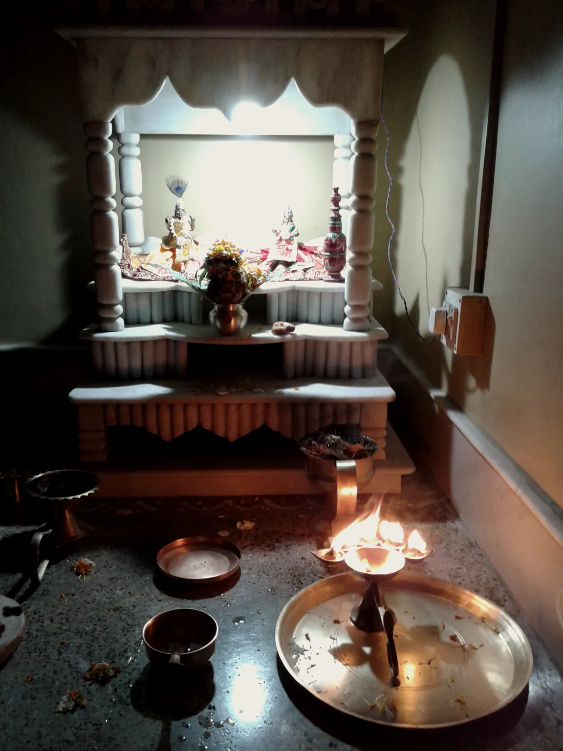A home mandir at dusk with a brass lamp lit before it