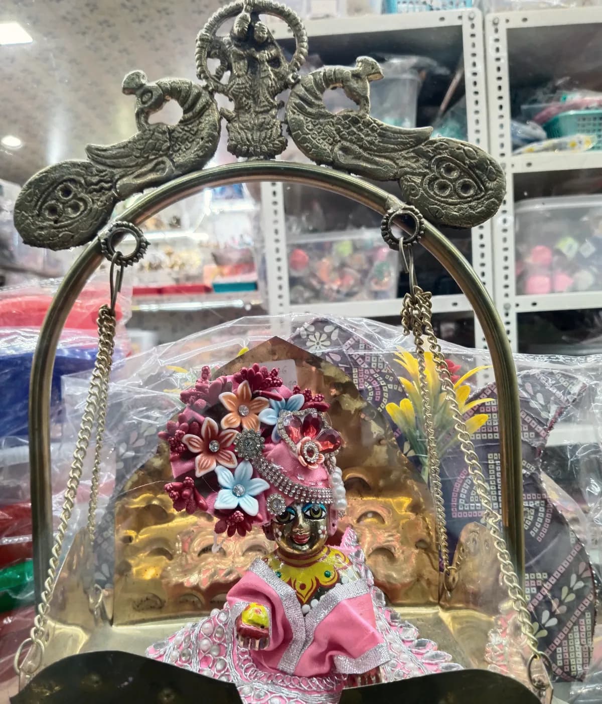 Laddu Gopal dressed in pink, seated in an ornate brass jhula