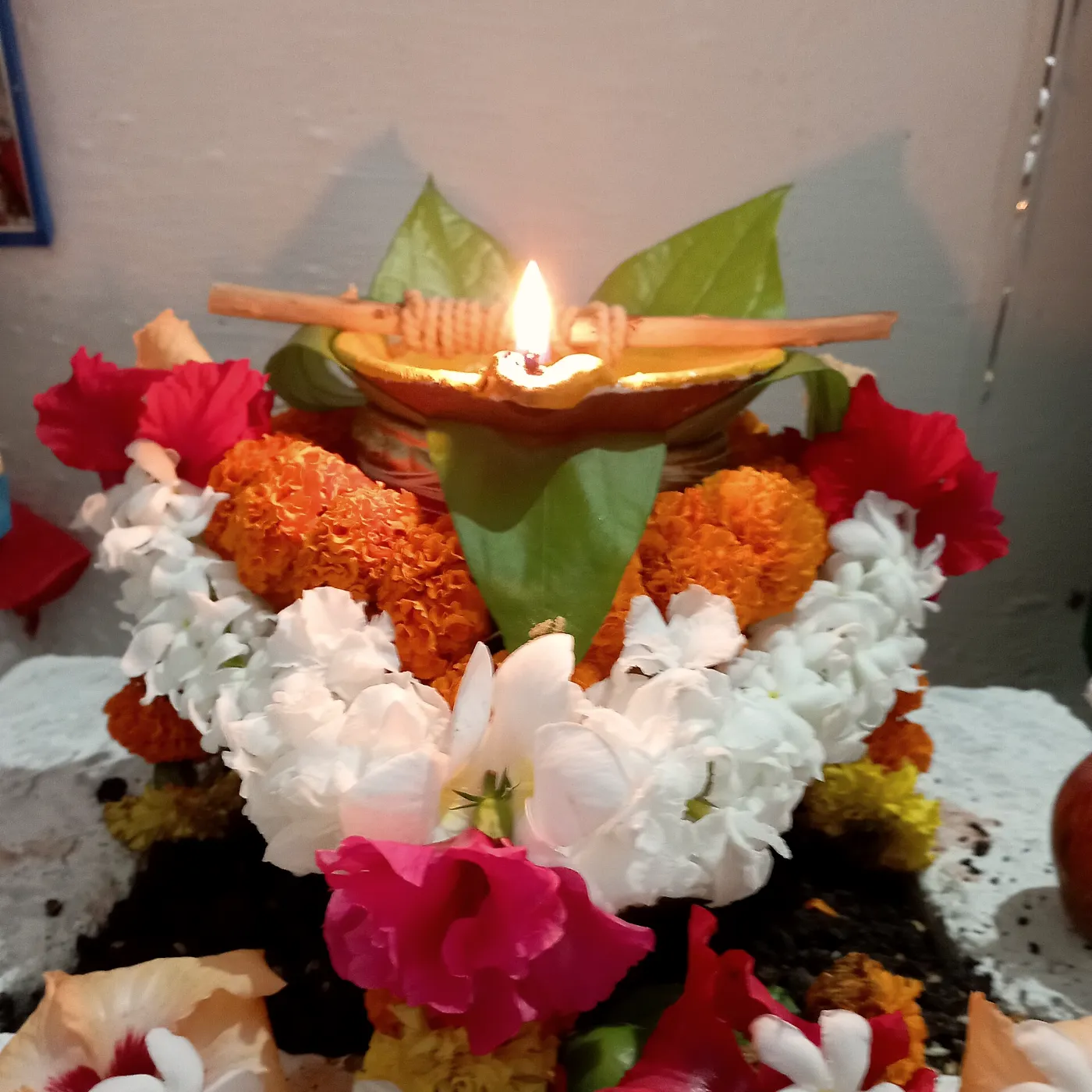 A kalash crowned with a lit diya and a bed of marigold and jasmine