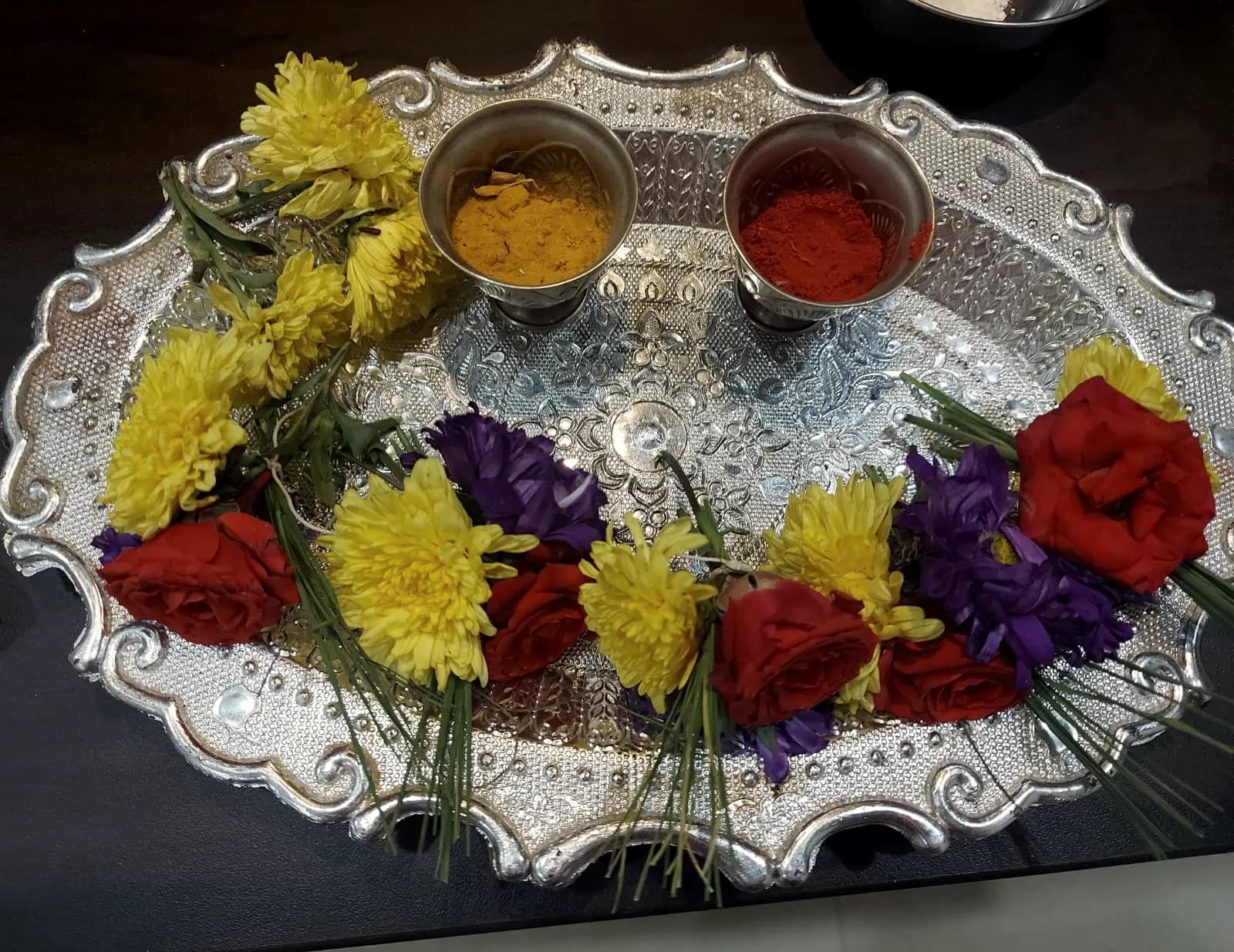 A silver puja thali with haldi, kumkum and fresh flowers